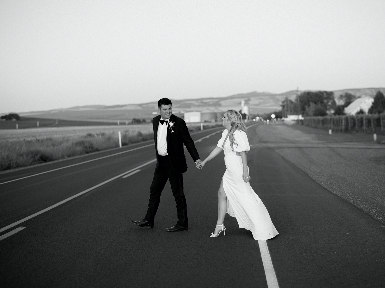 bride and groom walk across the road during sunset portraits
