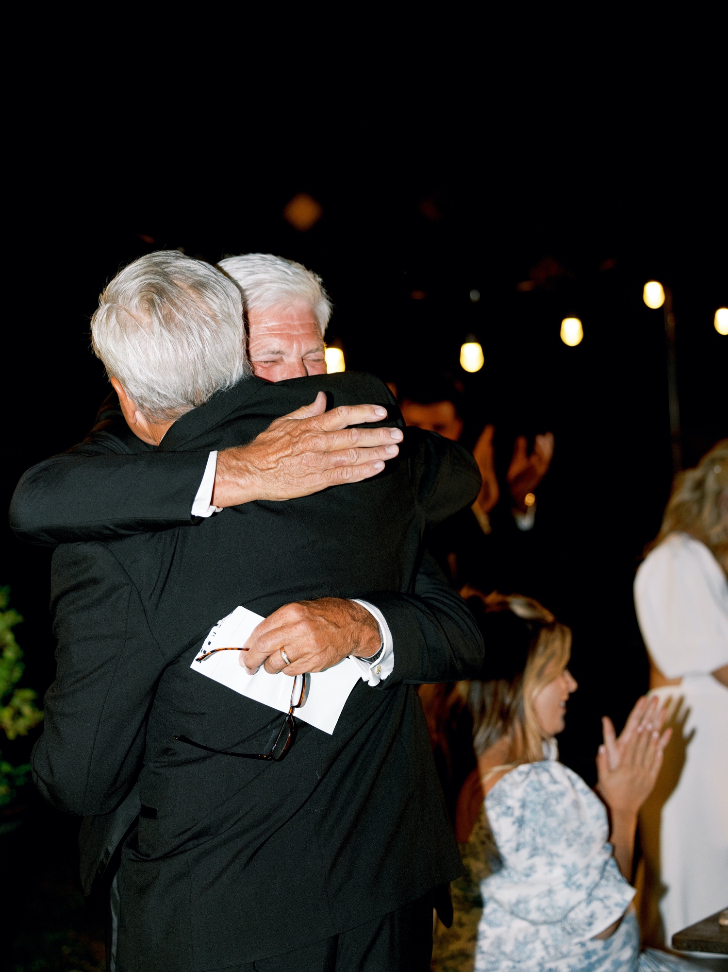 father of the bride and father of the groom share a hug of wedding toasts